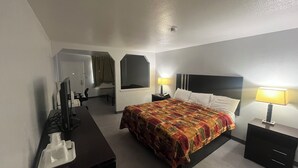 Ein Hotelzimmer mit einem Bett, zwei Nachttischen mit Lampen, einem Schreibtisch mit Telefon, einem Spiegel und einer Tür zu einem anderen Raum.