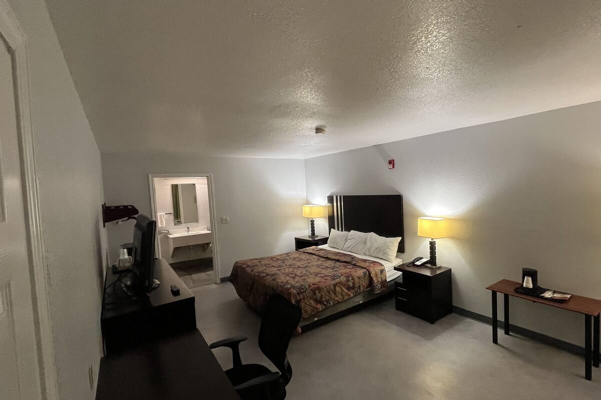 Une chambre d’hôtel comprenant un lit, des tables de chevet, un bureau avec une chaise, un miroir et une lampe.