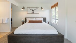 Een moderne slaapkamer met een groot bed, een hertenfoto in een lijst, twee wandlampen en een raam met jaloezieën.