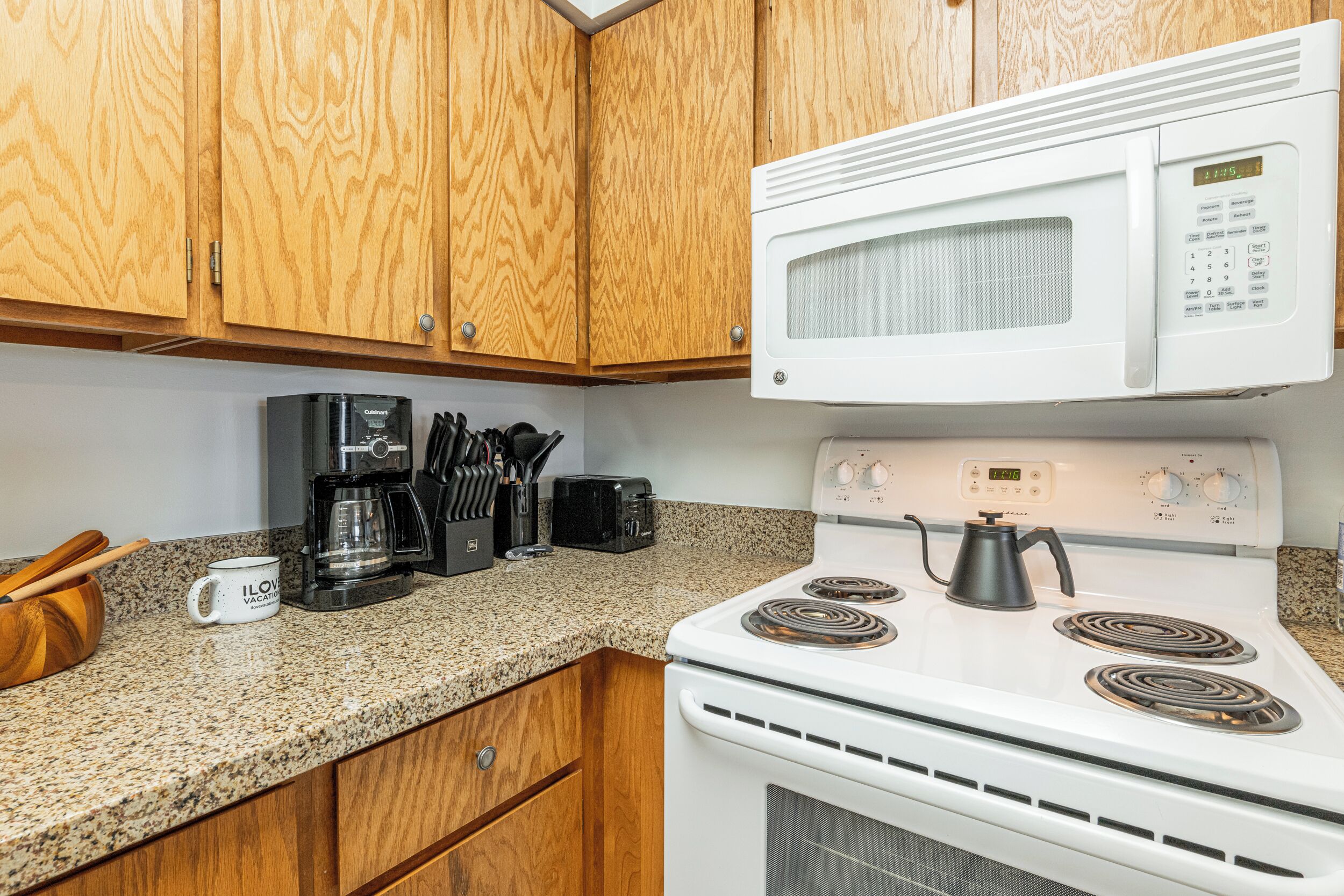 A kitchen with wooden cabinets, a white microwave, a stove with two burners, and a coffee maker.