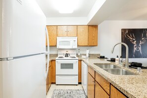 Una cocina compacta con electrodomésticos blancos, armarios de madera y encimeras de granito, además de un lavamanos grande.