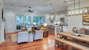 A spacious living area with a wooden floor, a dining table, and a kitchen in the background.
