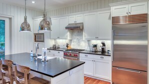 A modern kitchen with white cabinetry, stainless steel appliances, and a central island with bar stools.