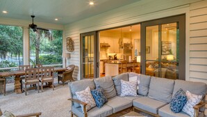 A spacious living area with a large sectional sofa, wooden furniture, and a view of the kitchen through glass doors.