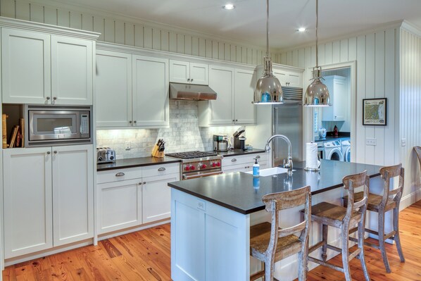 A kitchen with white cabinets, a central island with bar stools, stainless steel appliances, and pendant lighting.