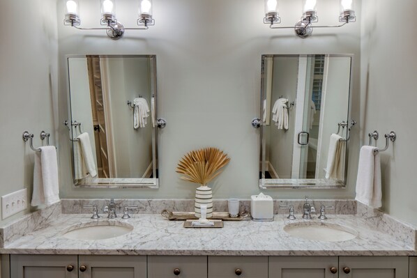 A bathroom with two sinks, two mirrors, and a vase with dried plants.