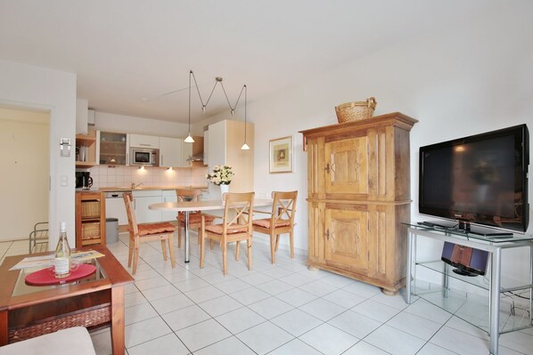 Une cuisine moderne avec des meubles blancs, une table à manger avec des chaises, un meuble en bois et un téléviseur à écran plat posé sur un meuble.