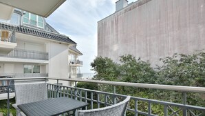 Ein Balkon mit Tisch und Stühlen, der auf ein Gebäude mit grauer Fassade und Meerblick blickt.
