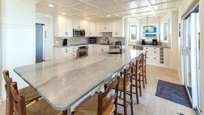 A spacious kitchen with a large island, white cabinetry, and a breakfast bar area. - Hobbs Realty - Very Last Home on the Island w/Heated Pool, Elevator, Luxury Amenities (Holden Beach)