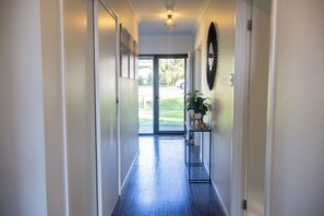 A hallway with a door leading to a glass door entrance, a potted plant on a console table, and a wall-mounted light fixture. - Bella Views Pet Friendly With Expansive Views (Mallacoota)