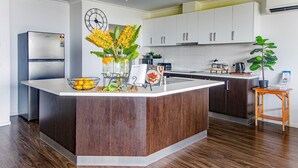 A modern kitchen with a central island, white cabinetry, a stainless steel refrigerator, and a wooden floor. - Bella Views Pet friendly with expansive views. (Mallacoota)