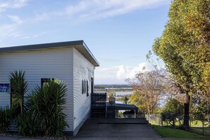 A single-story building with a flat roof, a covered outdoor area with a bench, and a view of a body of water. - Bella Views Pet Friendly With Expansive Views (Mallacoota)