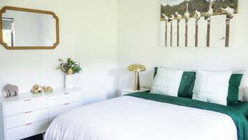 Ein Schlafzimmer mit einem Bett, einer Kommode, einem Spiegel, einer Lampe und einem Wandbild.