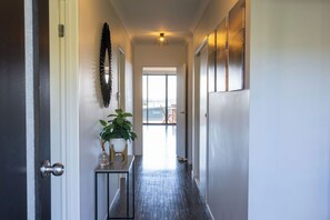 A hallway with a door on the left, a plant on a small table, and a large window at the end. - Bella Views Pet friendly with expansive views. (Mallacoota)