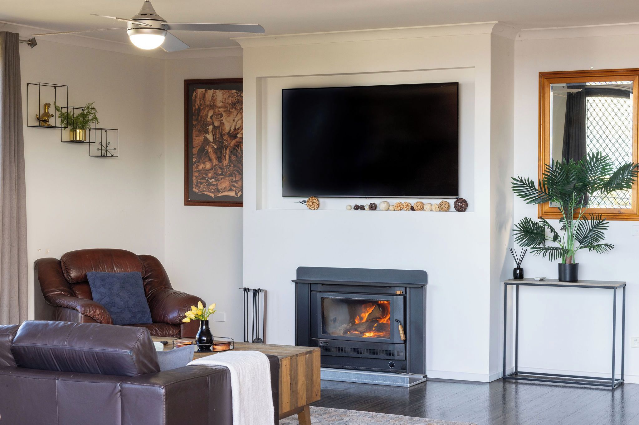 A living room with a fireplace, a large flat-screen TV, a leather armchair, and a potted plant.