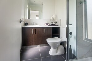 A modern bathroom with a white toilet, dark wood cabinets, a glass shower enclosure, and a mirror above the sink. - Bella Views Pet Friendly With Expansive Views (Mallacoota)