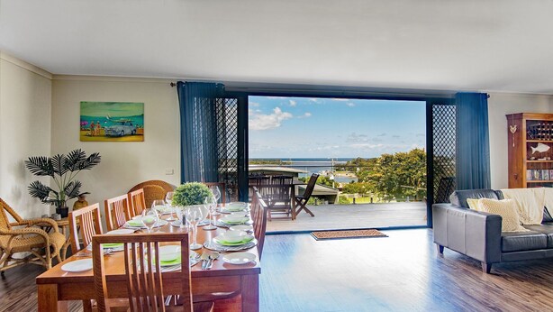 A dining area with a view of the sea, a balcony with outdoor furniture, and a living room with a sofa and a bookshelf. - Bella Views Pet friendly with expansive views. (Mallacoota)