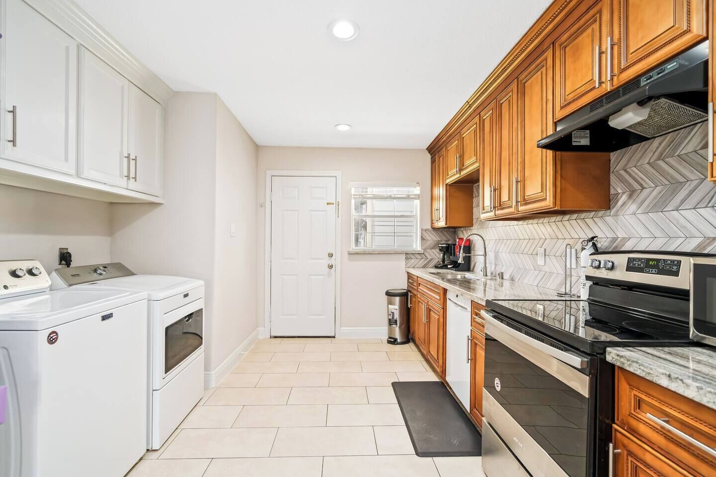 A kitchen with white appliances, wooden cabinets, and a herringbone tile backsplash.