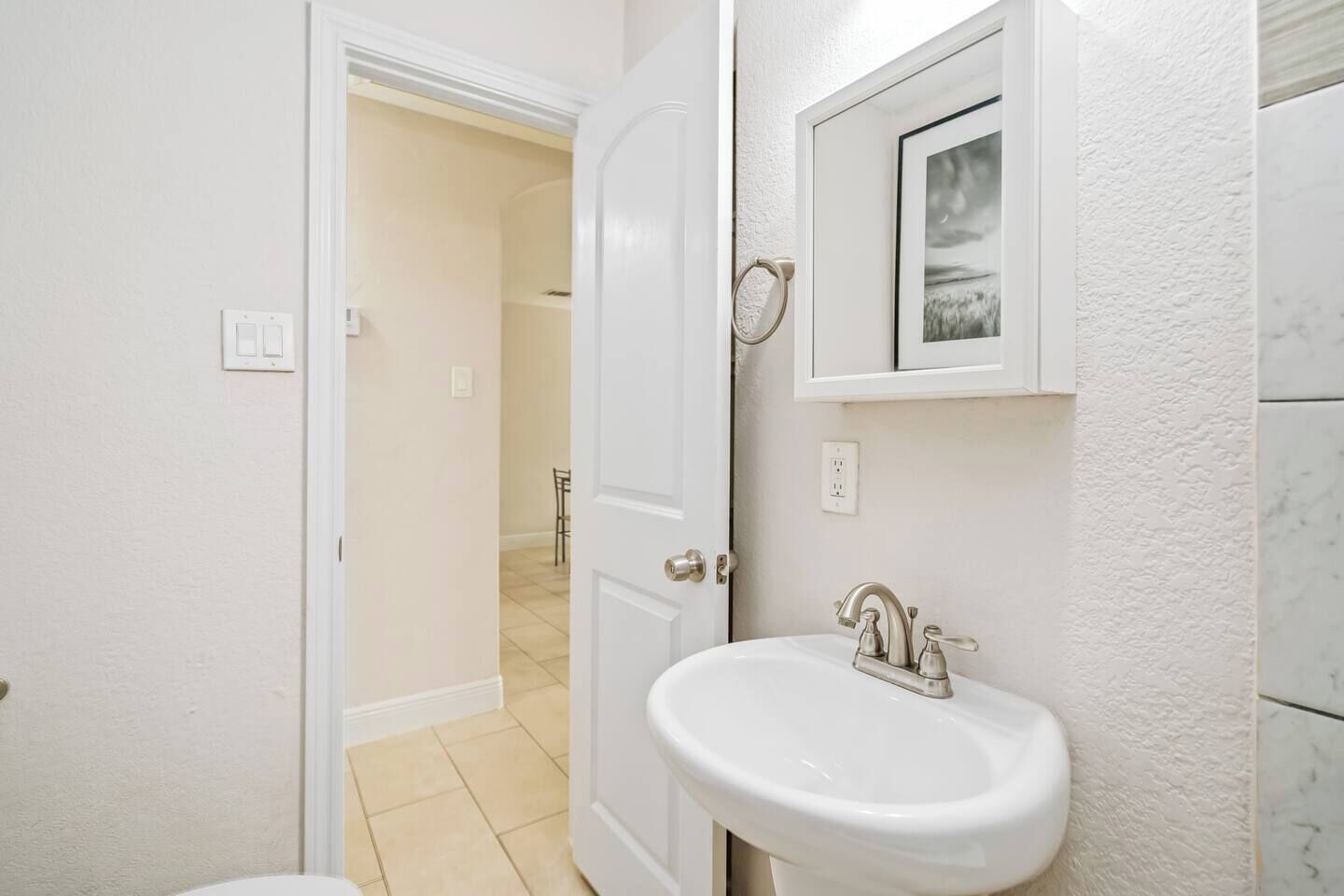 A bathroom with a white sink, a mirror, and a door leading to another room.