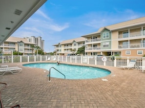 A swimming pool surrounded by a brick patio with lounge chairs and a fence.