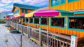 Een rij felgekleurde restaurants aan het strand, met terras en een houten dek.