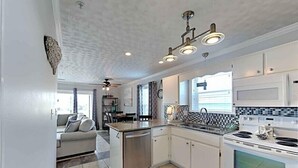 Een moderne keuken met witte kasten, een ingebouwde oven en een RVS fornuis. Er is een zithoek met een bank en een klein eiland.