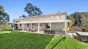 A modern house with a covered patio, outdoor seating, and a well-maintained lawn. - Kurrajong at Malua (Malua Bay)