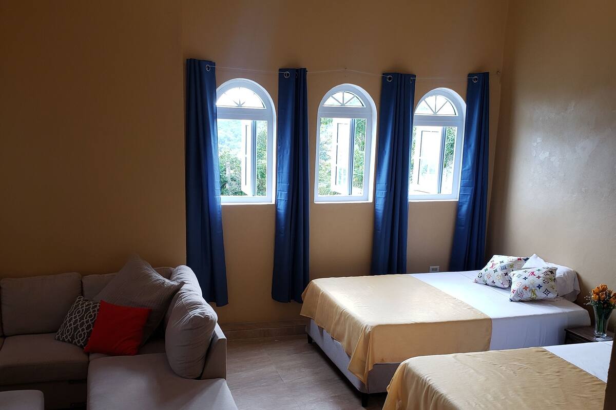 A room with two beds, a sofa, and a window with curtains.