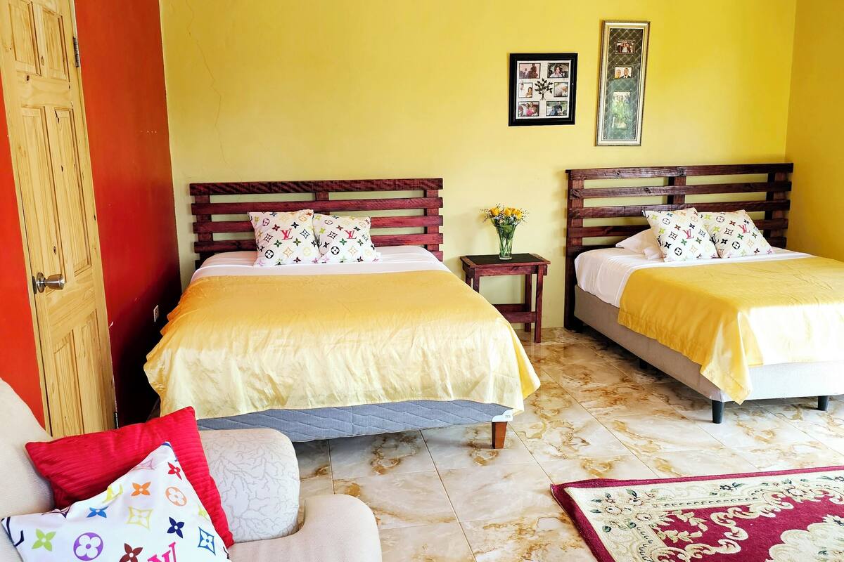 A hotel room with two beds, a wooden door, a small table with a vase, and a patterned rug.