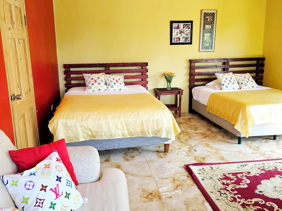 A hotel room with two beds, a wooden door, a small table with a vase, and a patterned rug.
