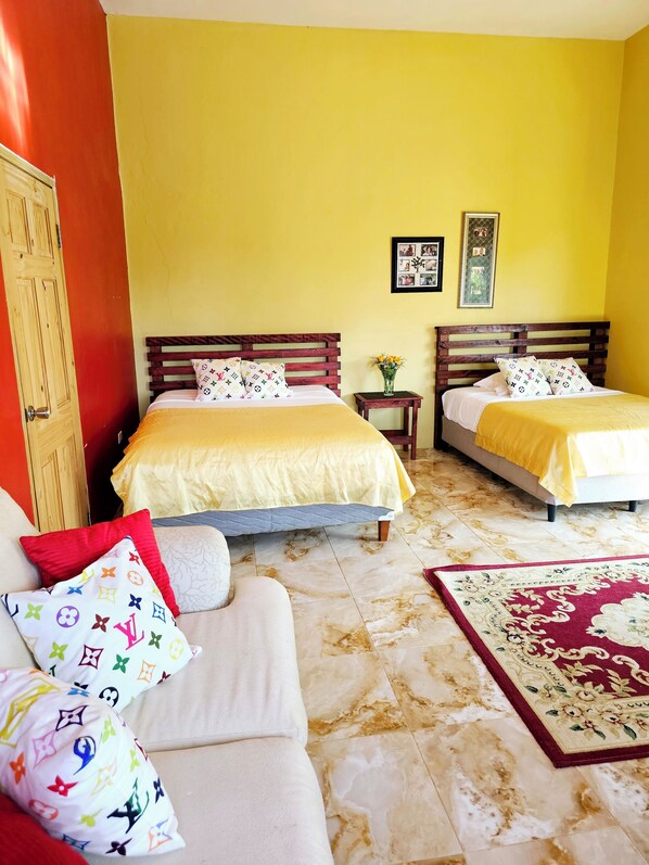 A hotel room with two beds, a wooden door, a small table with a vase, and a patterned rug. - Boston Bay (Port Antonio)