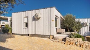 Un bâtiment moderne avec une entrée pavée de pierres, un espace extérieur abrité avec des sièges, et un ciel d’un bleu éclatant.