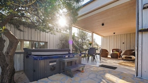 Un espace extérieur aménagé en terrasse, doté d’un jacuzzi, d’un revêtement de sol en pierre, d’une plateforme en bois et de mobilier de jardin.