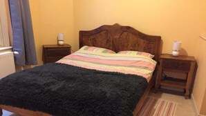 A bed with a dark furry blanket, wooden headboard, and striped bedding. There are two bedside tables with lamps and a small rug on the floor.