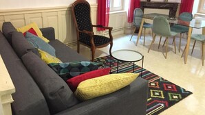 A living room with a sofa, chairs, a small round table, and a dining area with a glass table and chairs.