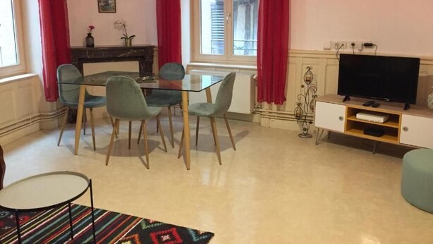 A dining area with a glass table and chairs, a television on a wooden stand, and red curtains.