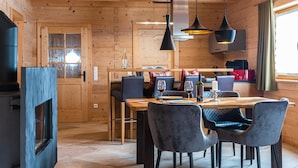 A wooden interior with a dining area featuring a wooden table and chairs, a kitchen area with a stove, and pendant lighting. - Luxury design chalet category 1, 105sqm, 2 separate bedrooms, Swiss stone pine furniture (Ruhpolding)