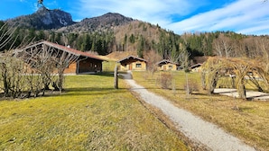 A row of rustic cabins with a gravel path leading to them, surrounded by a forested mountain backdrop. - Luxury design chalet category 1, 105sqm, 2 separate bedrooms, Swiss stone pine furniture (Ruhpolding)