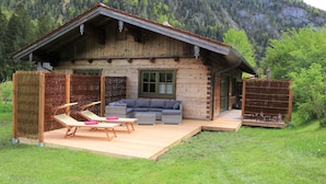 A wooden cabin with a deck, outdoor seating, and a view of a forested mountain. - Luxury design chalet category 1, 105sqm, 2 separate bedrooms, Swiss stone pine furniture (Ruhpolding)