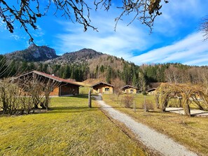 A row of rustic cabins with a gravel path leading to them, surrounded by a forested mountain backdrop. - Luxury log cabin made of natural logs, 165 m², 3 bedrooms, 2 bathrooms, fireplace, terrace with hot tub (Ruhpolding)
