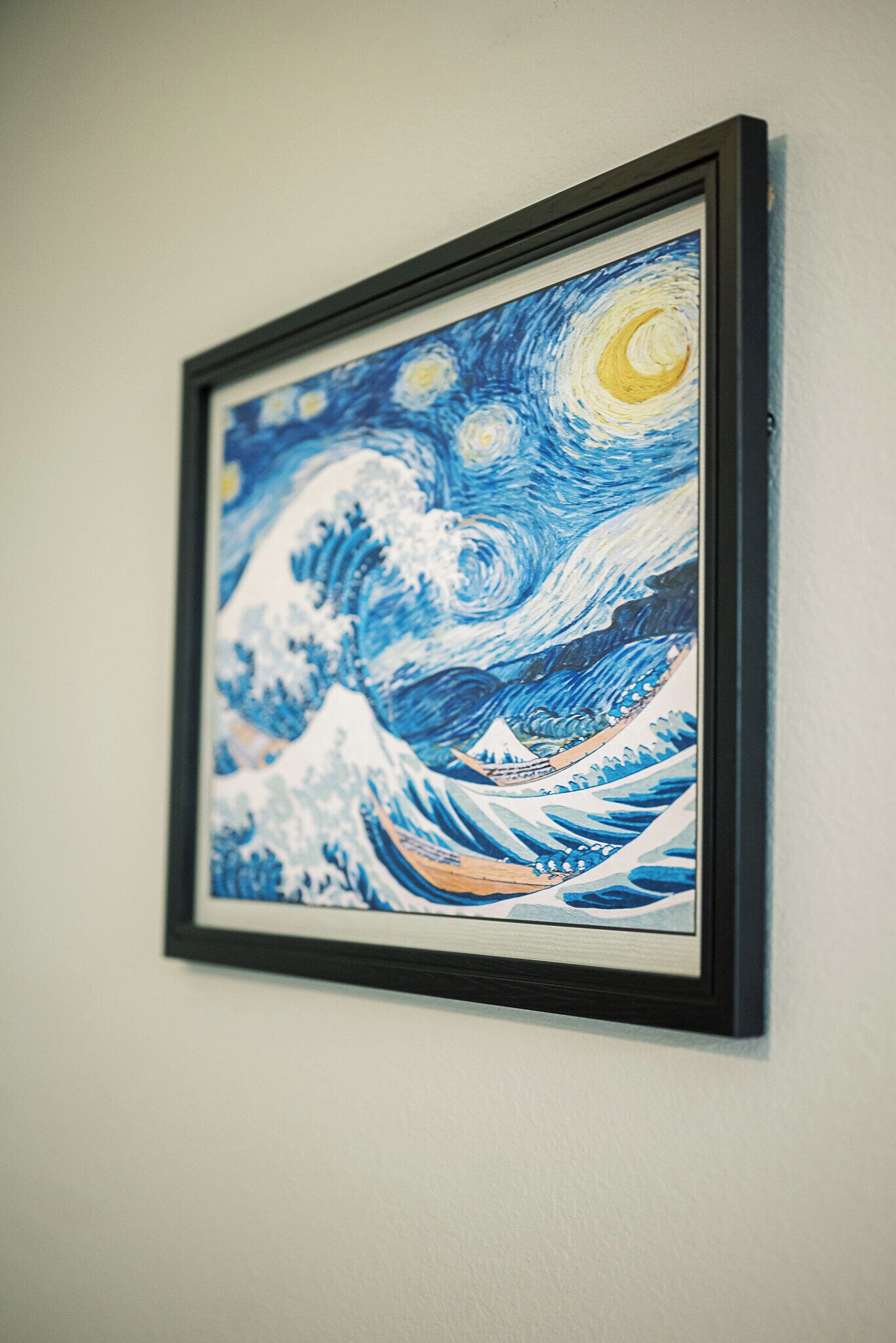 Une œuvre d’art encadrée représentant une vague, avec une lune et des étoiles, accrochée à un mur.