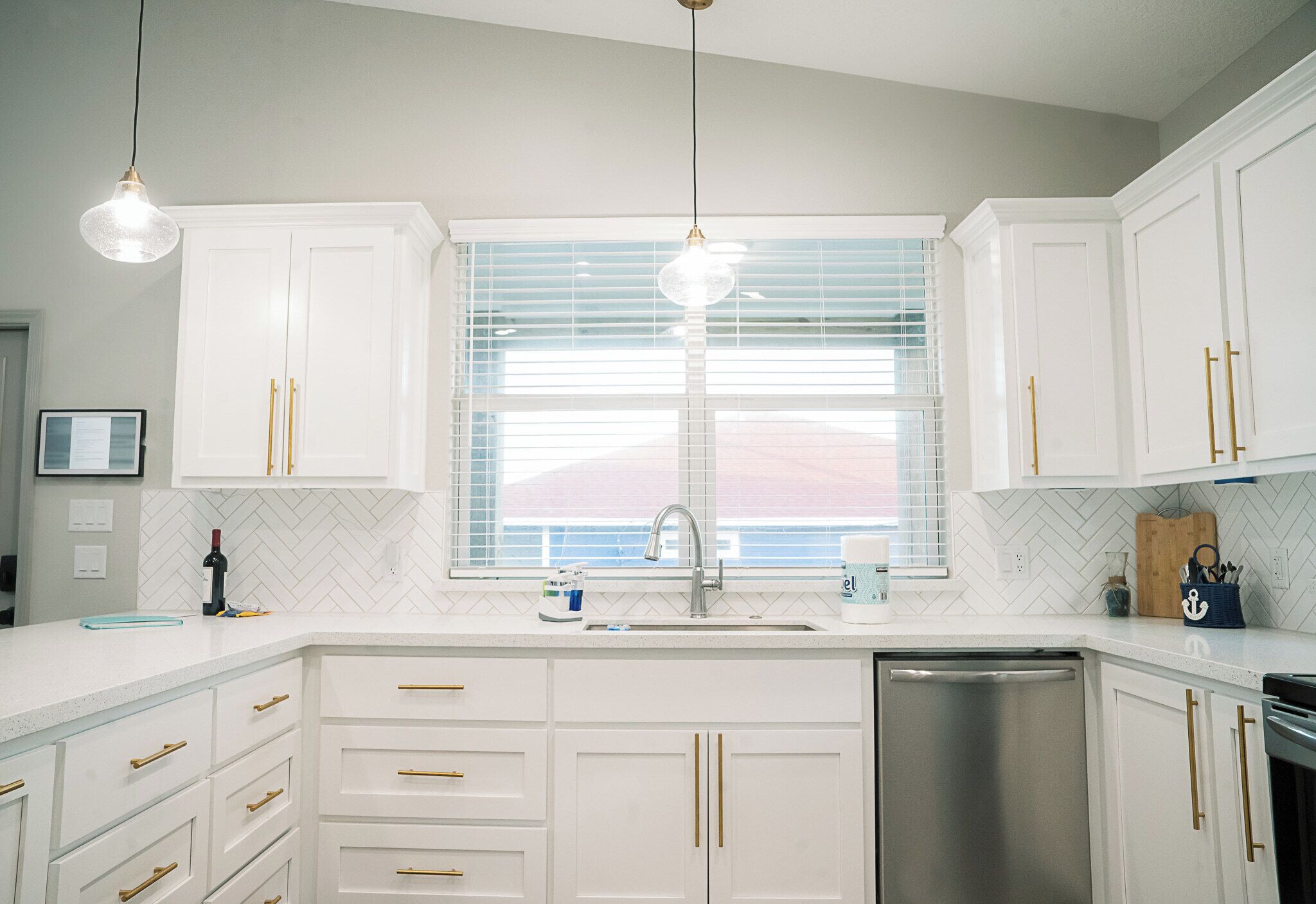 A kitchen with white cabinets, a stainless steel dishwasher, and a window with blinds.