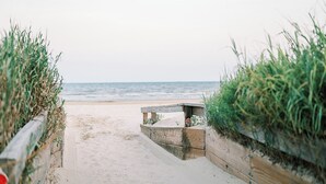 Un sendero de arena que conduce al mar, bordeado por barreras de madera con vegetación.