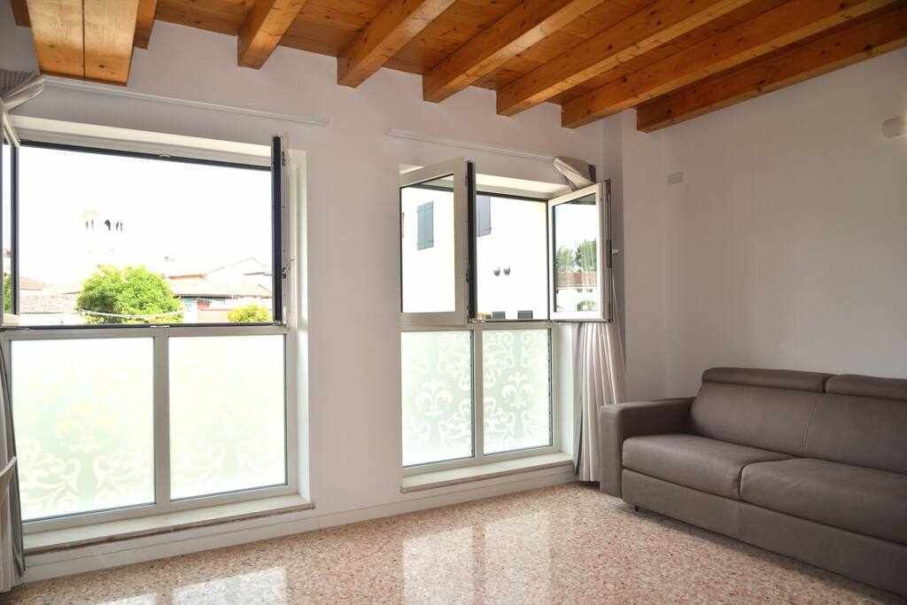 Ein Zimmer mit großem Fenster, einer Couch und einer Holzbalkendecke.