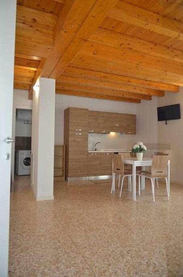 A modern kitchen with wooden cabinets, a dining area with white chairs, and a built-in TV. - Palazzo Maggiore Suite B (Noale)