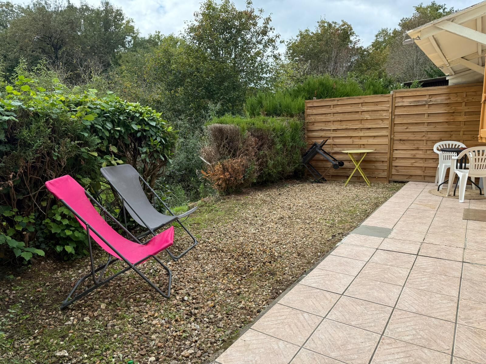 Un espace patio comprenant une chaise noire et rose, une petite table et deux chaises blanches.