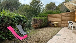 Un espacio al aire libre con una silla negra y rosa, una mesita y dos sillas blancas.