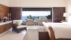 Une chambre d’hôtel avec un lit, deux fauteuils, une petite table et une vue sur l’océan.