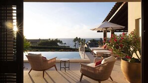 Un espace aménagé au bord de la piscine, avec des fauteuils en osier, une petite table et une grande plante en pot.