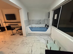 Un bagno moderno con una grande vasca, una TV a parete e un'area relax con sedie.